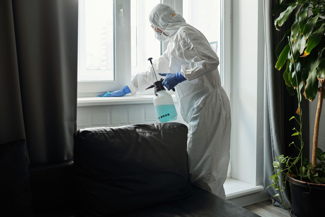 services-01 Person in PPE disinfecting indoor window area during COVID-19 pandemic.